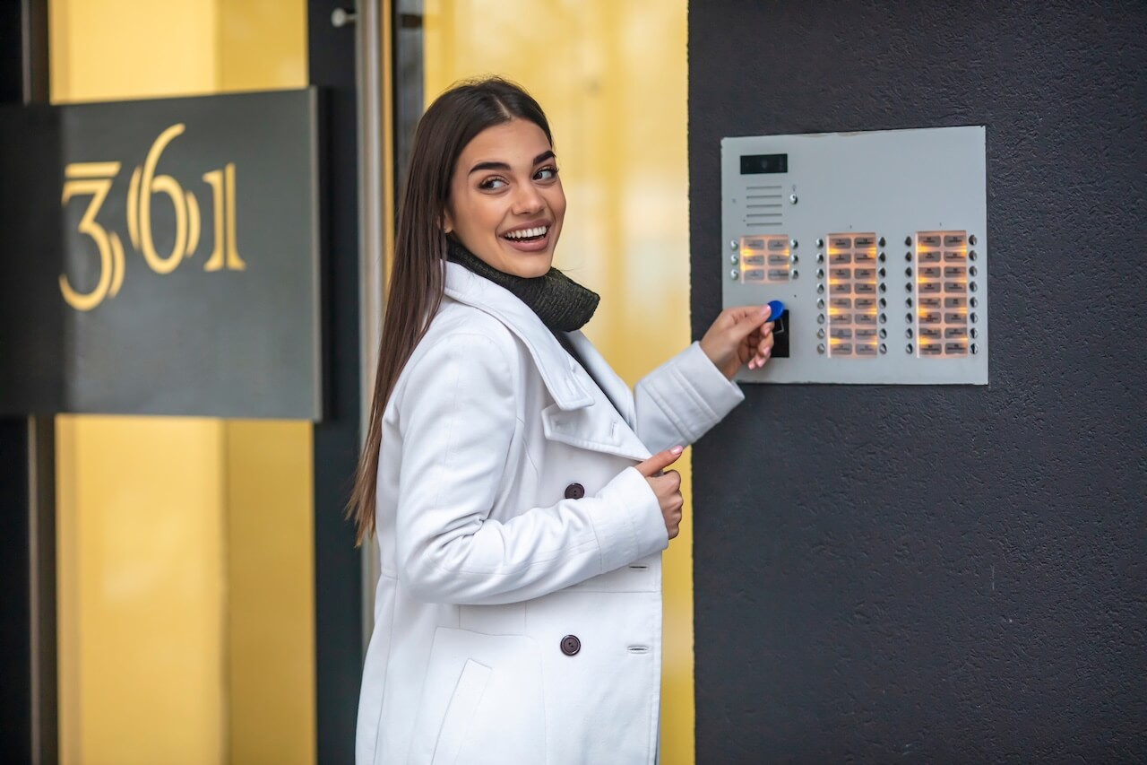 Young business woman in white suit touching the intercom with keyfob