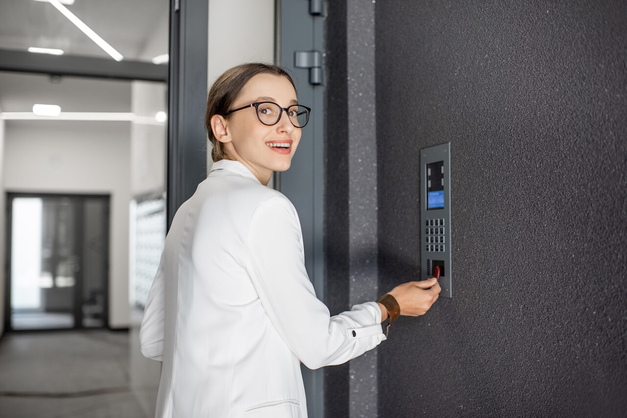 woman in white suit touching the intercom with keychain opening the door of residential modern building