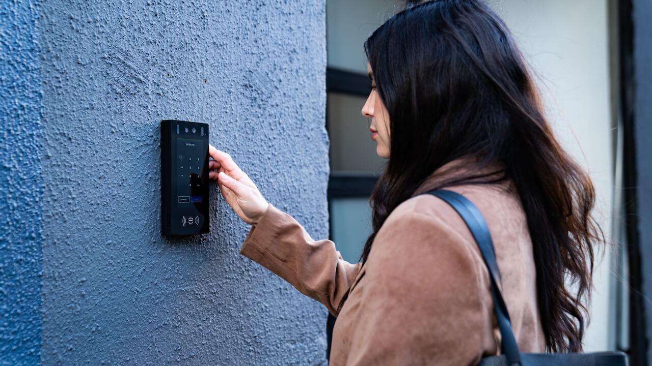 woman using the intercom mounted on a grey wall