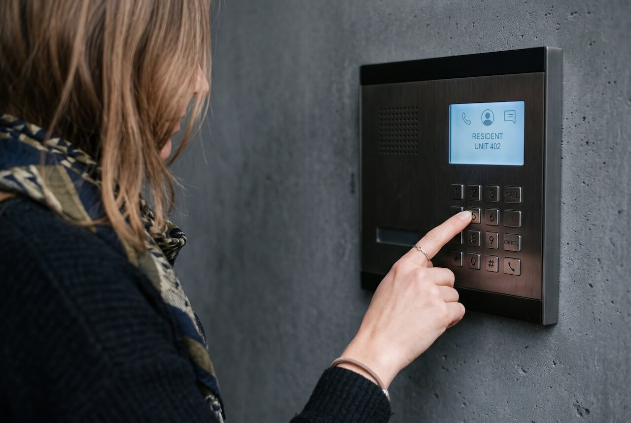 Woman pressing a button on a modern digital intercom system mounted on a grey concrete wall