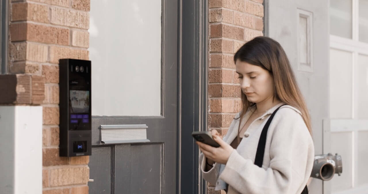 Woman using a mobile phone app to access a building intercom panel