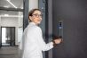 woman in white suit touching the intercom with keychain opening the door of residential modern building