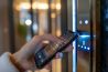 woman entering password code on the smart phone and digital touch screen keypad entry door lock in front of a hotel room