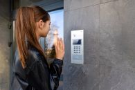 woman uses an outdoor intercom panel at a modern apartment entrance for secure access