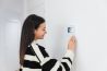 Happy young woman using apartment intercom at home